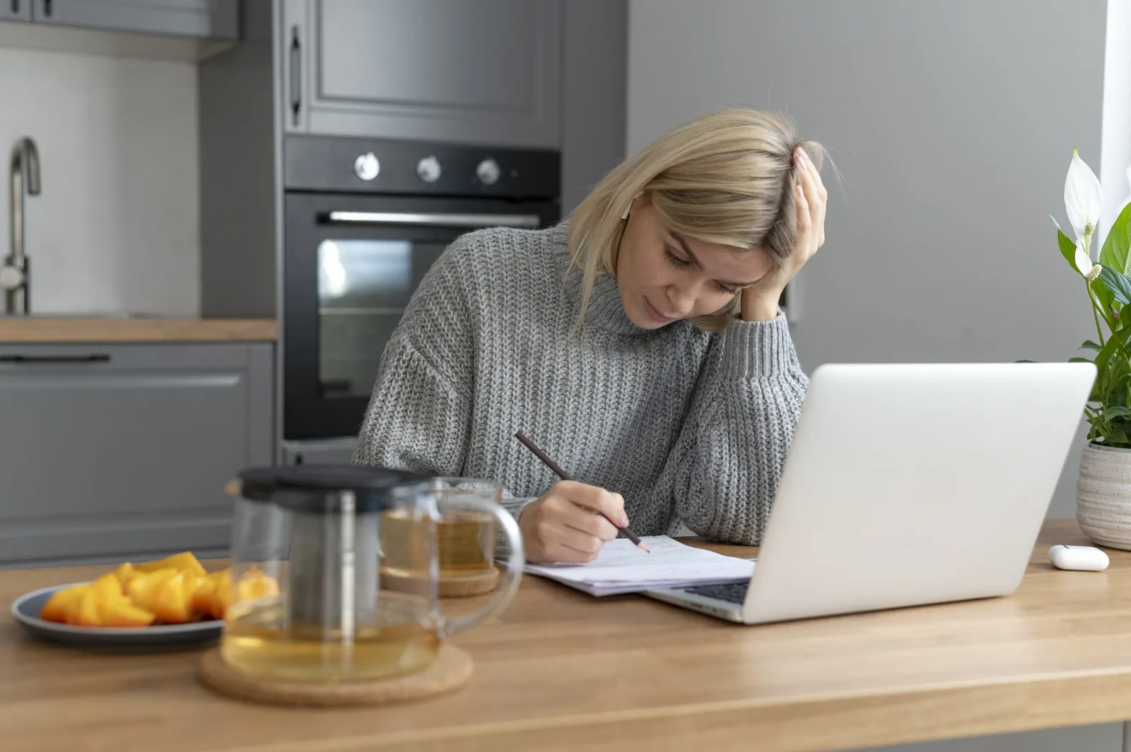 Person vid köksbord med laptop och papper som räknar på sin ekonomi, illustrerar a-kassa 2026 villkor och belopp